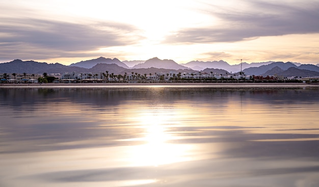 The landscape sky is reflected in the sea in the setting light. City coastline with mountains on the horizon.