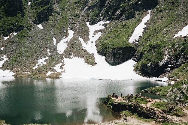 ルーマニアのバレア湖と雪に覆われたピークを持つ夏のフグラシ山の風景を見る