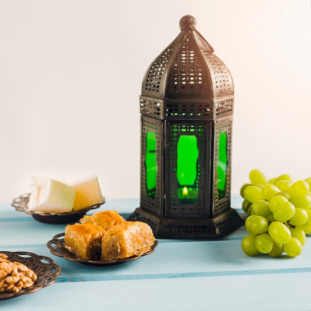 Lantern near green grape with baklava and Turkish delights on saucers