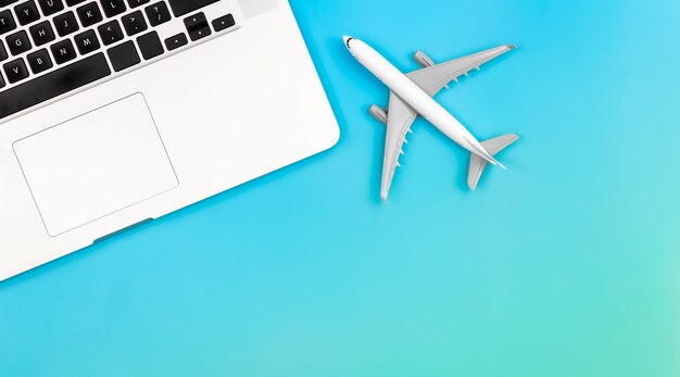 Laptop and airplane miniature on blue background flat lay copy space