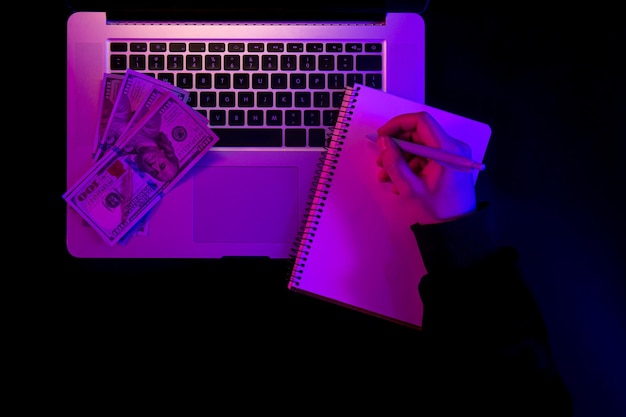 Foto gratuita blocco note in bianco del computer portatile e soldi di carta nella vista superiore di illuminazione al neon