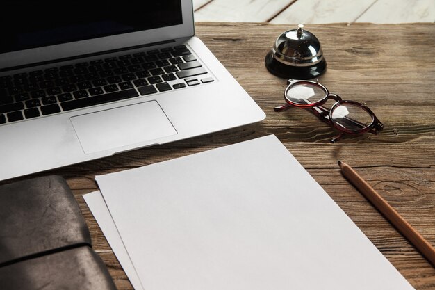 The laptop, blank paper, glasses and small bell on the wooden table