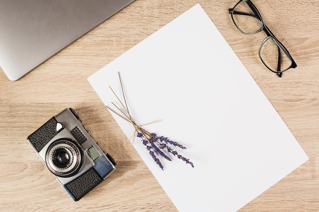 Laptop; camera; eyeglasses and blank paper with lavender twig on wooden table