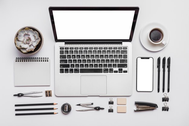 Laptop; cellphone; cup of coffee and office stationery on white background