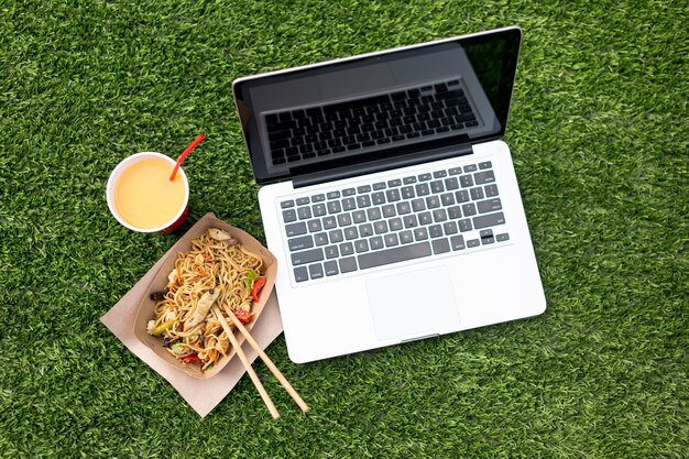 Laptop and chinese food on grass background