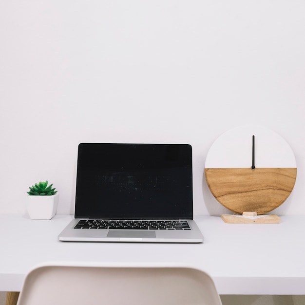 Laptop between clock and plant on table