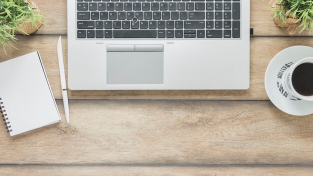 Laptop and coffee cup near notebook on table