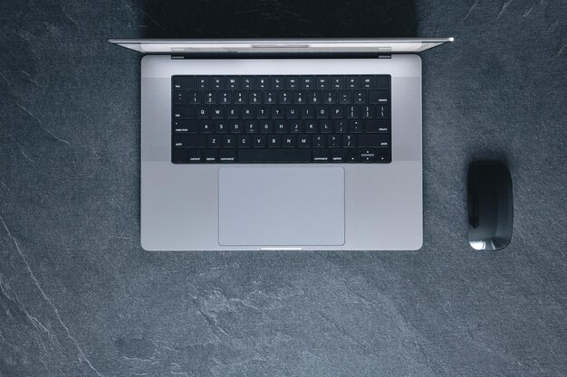 Laptop and computer mouse on a dark textured background top view