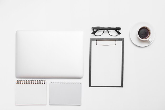 Laptop; cup of black coffee and office stationeries isolated on white backdrop