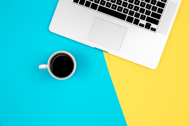 Free photo laptop and cup of coffee on a yellow and blue background flat lay