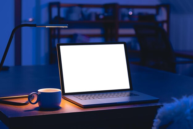 밤에는 빈 화면이 있는 어두운 방의 테이블 위에 노트북과 컵