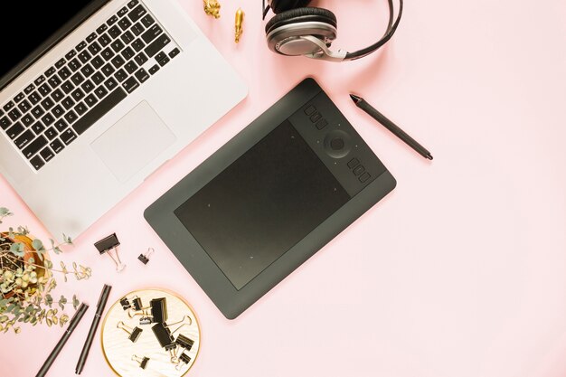 Laptop and digital graphic tablet with headphone on pink backdrop