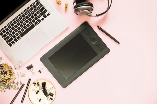 Ноутбук и цифровой графический планшет с наушниками на розовом фоне