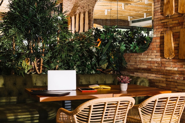 Laptop; digital tablet; book and pot plant on wooden table in the restaurant