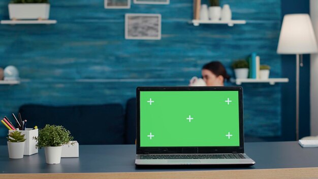 책상에 녹색 화면 배경이 있는 노트북 디스플레이, 격리된 크로마 키가 있는 모형 템플릿 및 빈 복사 공간을 만드는 데 사용됩니다. 거실에서 컴퓨터에 현대 기술입니다.