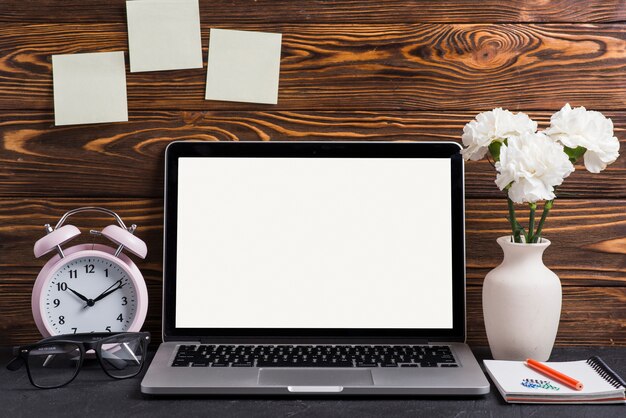 Laptop displaying white screen with vase; pencil and notepad on desk