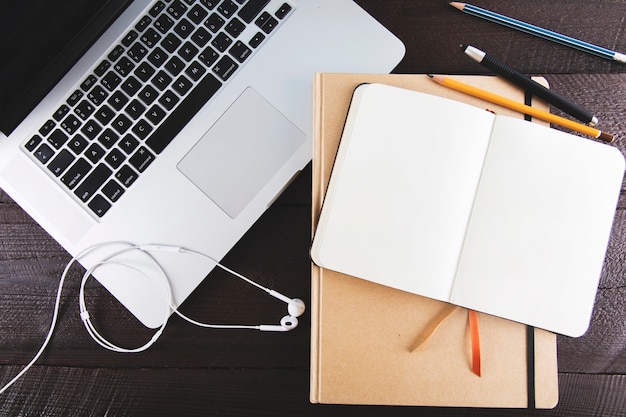 Laptop and earphones near notepads and pencils