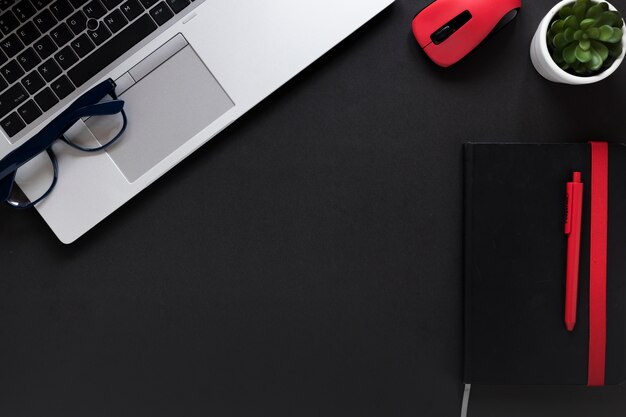 Laptop; eyeglasses; mouse; diary; pen and pot plant on black background