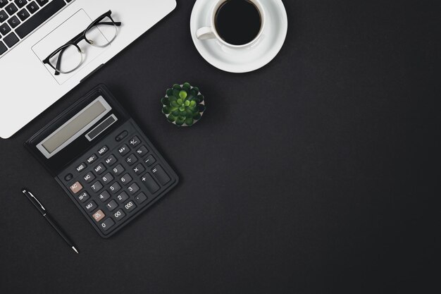 Laptop glasses coffee cup and calculator on a black background top view