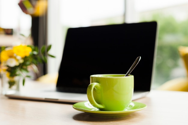 仕事机の上のノートパソコンと緑のセラミックコーヒーカップ