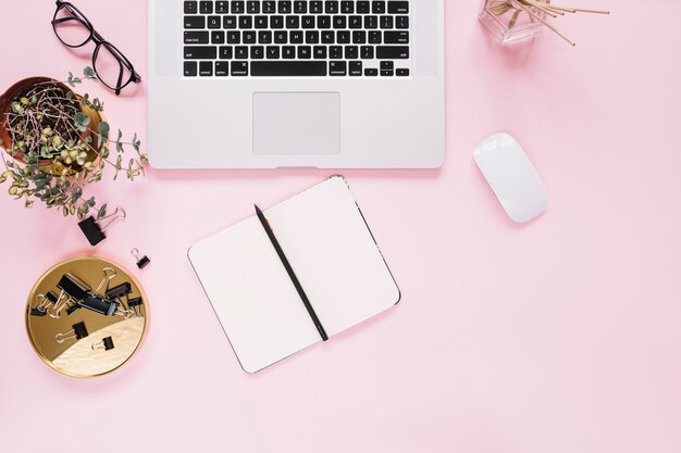 Laptop and mouse with diary and pen on pink backdrop