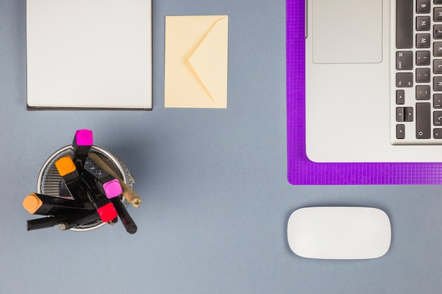 Laptop near paper, cup with felt pens, letter and computer mouse 