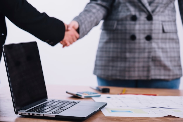 Laptop near people shaking hands