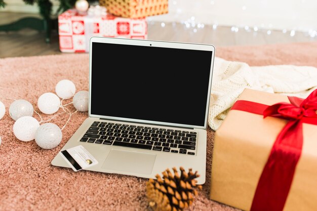 Laptop near plastic card, present boxes, fir snag and fairy lights