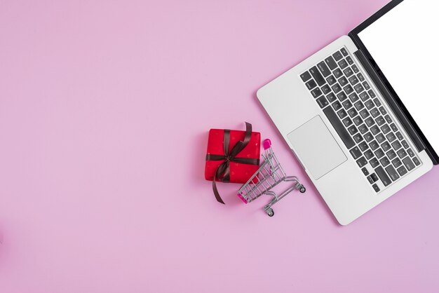 Laptop near tiny shopping cart and present