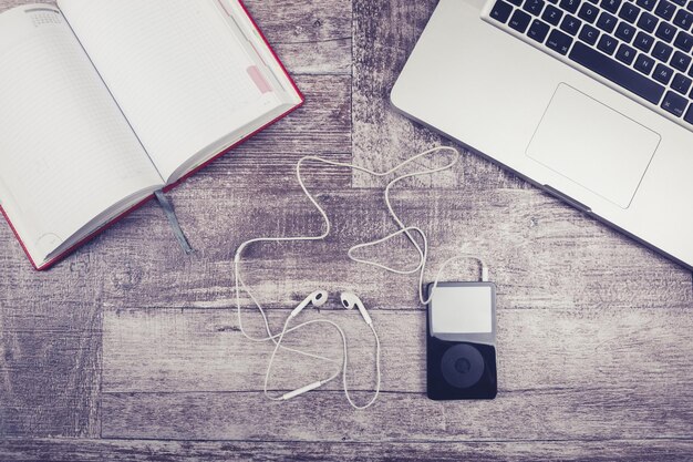 Laptop, notebook for writing and music player from above view on a wooden background