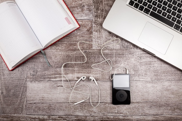 Laptop, notebook for writing and music player from above view on a wooden background