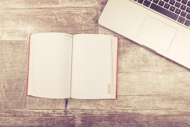 Laptop and a notebook for writing in vintage tone from above view on a wooden background