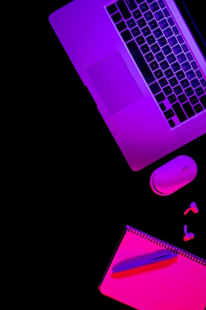 Free photo laptop and notepad on black background with neon light flat lay