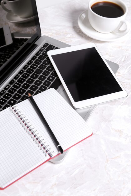 한 잔의 커피와 다른 장치가있는 테이블에 노트북, 메모장 및 펜