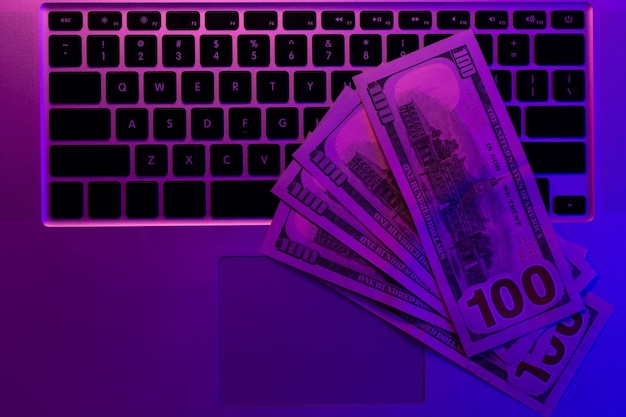 Free photo laptop and paper money in neon lighting top view