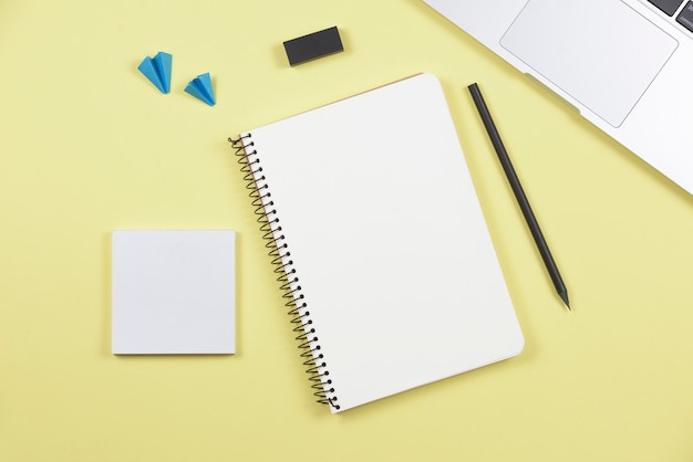 Free photo laptop; pencil; spiral notebook; adhesive notepad; airplane and eraser on yellow background