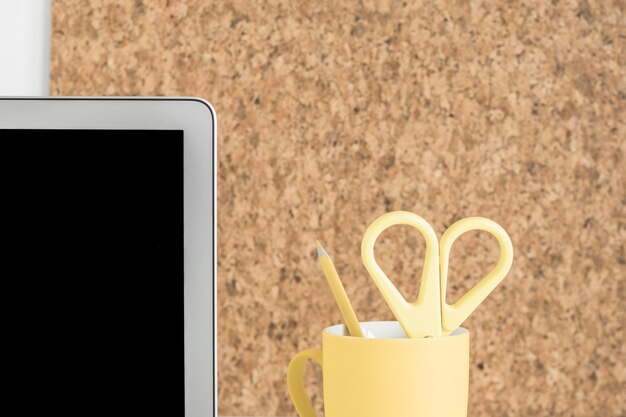 Экран ноутбука с ножницами и карандашом в держателе для чашки против пробковой доски