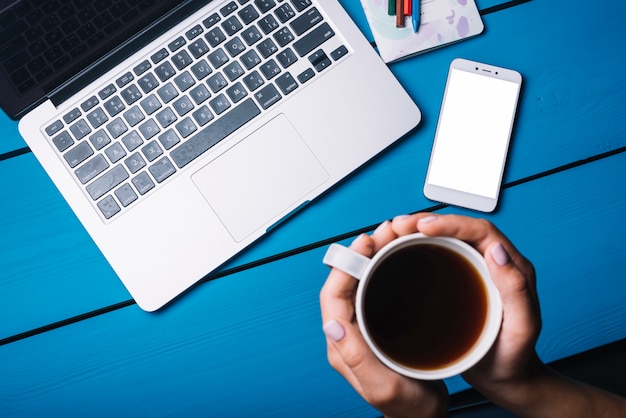 Laptop and smartphone on blue desk with coffee