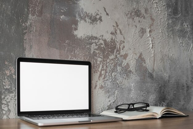 Laptop; spectacles and book on wooden tabletop