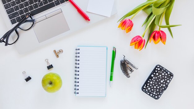 Laptop and stationery near tulip flowers and apple