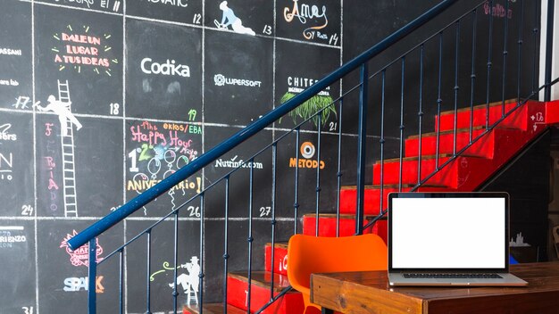 Laptop on table in front of staircase and decorative wall