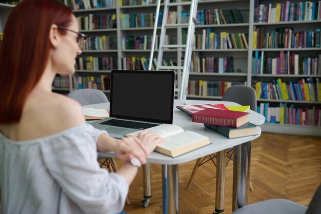 テーブルの上のラップトップと本を読んでいる女性