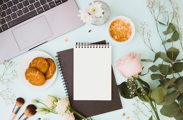 Laptop; vase; bouquet; makeup brush; cookies and golden pushpin on blue background