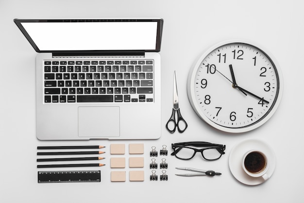 Il computer portatile; orologio da parete; tazza di caffè e cancelleria per ufficio su sfondo bianco