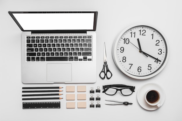 ноутбук; настенные часы; чашка кофе и канцелярские принадлежности на белом фоне