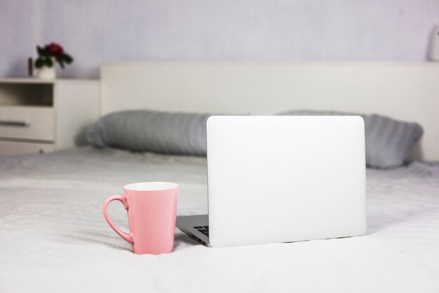 Laptop on white bed with coffee cup