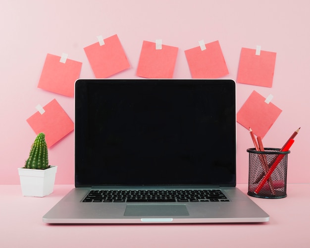 Laptop with blank black screen on pink office desk