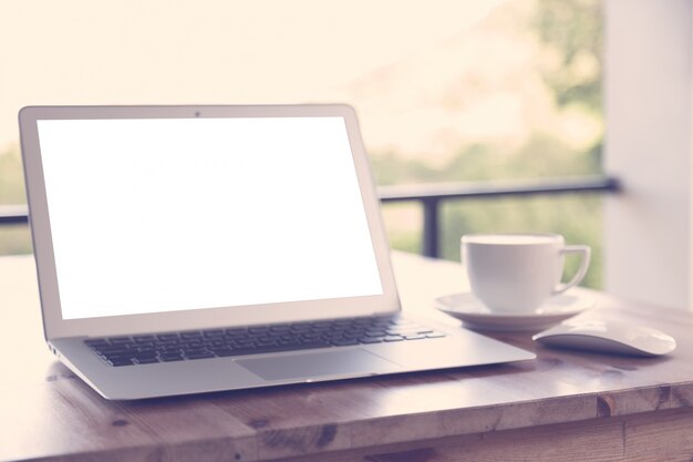 Laptop with blank screen on a wooden table and a cup of coffee