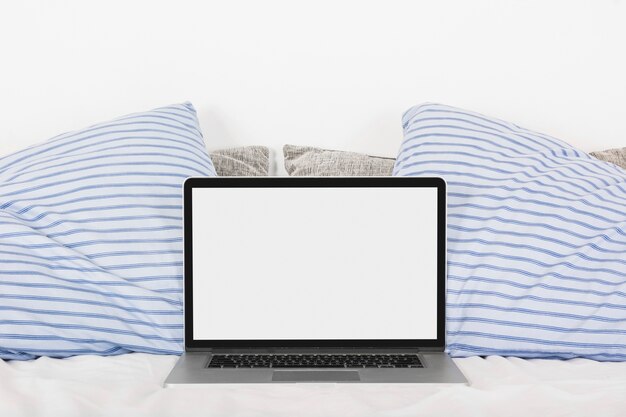2つの枕が付いたベッドに白いスクリーンが空いているラップトップ