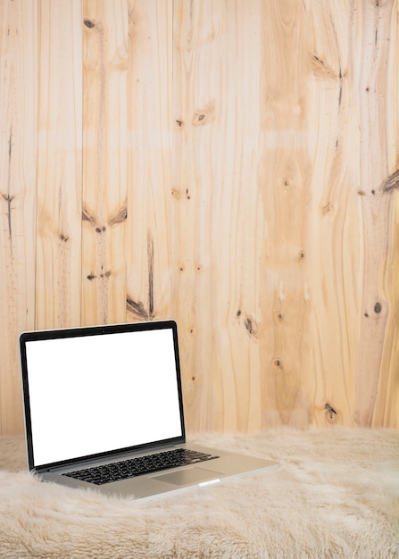 Foto gratuita computer portatile con schermo bianco vuoto su morbida pelliccia davanti alla parete di legno